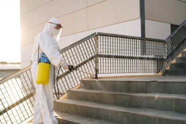 Virüs korumalı giysili bir adam binaları spreyle dezenfekte ediyor..