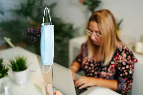 Mujer joven trabajando en una oficina con máscara protectora y distancia social — Foto de Stock