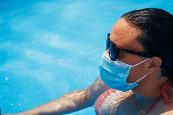 Een vrouw badend in een zwembad met een zonnebril en een masker. Covidieuze pandemie. — Stockfoto