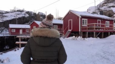 Norveç köyünün karlı, kırmızı ahşap kulübesinde yürüyen genç bir kadın.