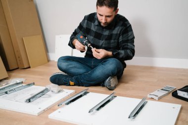 Yerde oturan bir adam bir parça mobilya monte ediyor. Kendin yap.