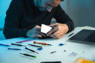 Teknisyen, masadaki akıllı telefon ekranını ve bataryayı tamir etmeye ve değiştirmeye hazırlanıyor.