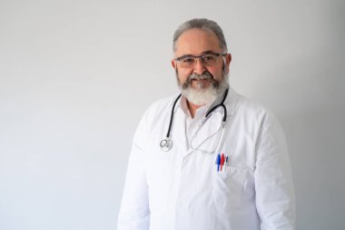Beyaz önlüklü yaşlı sakallı doktor portresi ve beyaz arka planda fonendoskop..