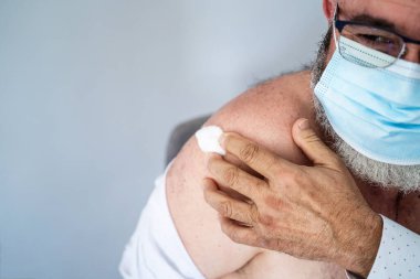 Cerrahi maskeli kıdemli adam geçenlerde Covid-19 aşısıyla aşılandı.