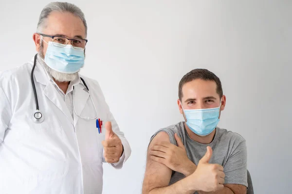 Médico y paciente con máscara quirúrgica contentos con los pulgares hacia arriba después de vacunar a su paciente con la vacuna covid-19 — Foto de Stock