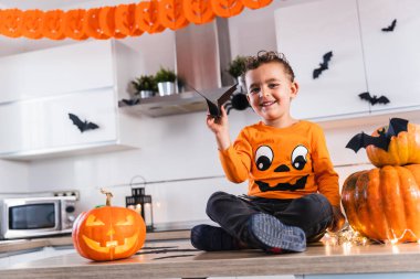 Cadılar Bayramı tişörtü giymiş yakışıklı bir çocuk Cadılar Bayramı için balkabağı açıyor ve onu Cadılar Bayramı partisi için süslüyordu.