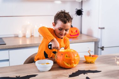 Cadılar Bayramı için balkabağı tişörtü giymiş küçük şirin bir çocuk Cadılar Bayramı için balkabağı boşaltıyor ve Cadılar Bayramı partisi için dekore ediyor. Mutlu Cadılar Bayramı