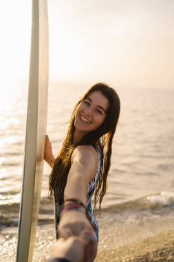 Mutlu kadın sörf tahtası ile el ele tutuşuyor, yaz macerasına davet ediliyor.