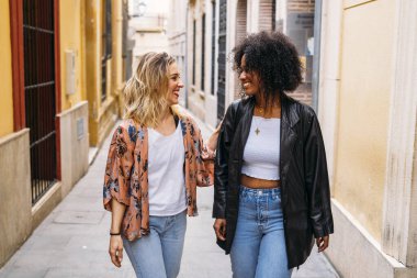 İki çok ırklı kadın arkadaş şehir sokaklarında yürüyüş yapıyorlar.