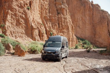 Kuru bir kanyonda kum ve engebeli kaya oluşumlarıyla seyahat eden bir karavan.