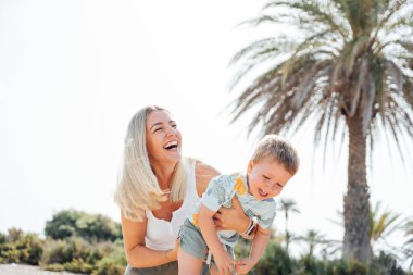 Anne kucağında çocuk, hem gülüyor hem de dışarıda eğleniyor.