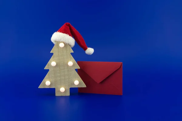 Gestileerde Houten Kerstboom Met Een Kerstmuts Bovenop Een Rode Envelop — Stockfoto