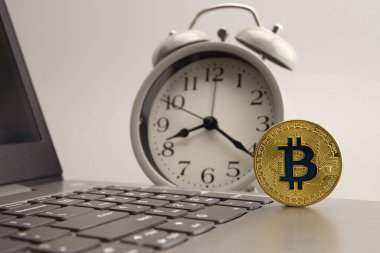 Çalar saatin yanındaki bilgisayar klavyesinde altın Bitcoin var. Dijital veya sanal para birimi kavramı, seçici odak