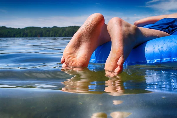 Wet bare feet of a person floating on an inflatable mattress in a swimming pool in summer showing dimpled skin from long immersion in the water in a concept of the seasons or vacation