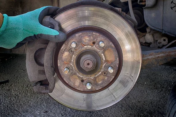 Car disk brake pad replacement service with hand of mechanic, brake disc rotor without wheels