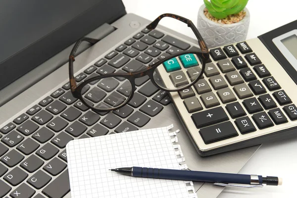 Office workstation with laptop, eyeglasses, notepad, calculator and pen in a close up high angle view in a business or accounting still life