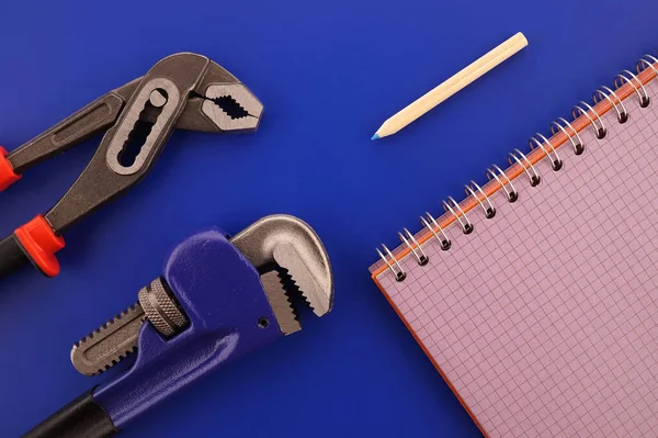 Renovation, production, manufacturing, building or repairs flat lay concept with an arrangement of two assorted wrenches and note books in a blue and red theme