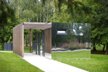 Aynalı duvarları olan çağdaş bir bina çevreleyen yeşilliği yansıtır ve şaşırtıcı bir görsel efekt yaratır. Yapı yemyeşil bir parka kurulmuş..