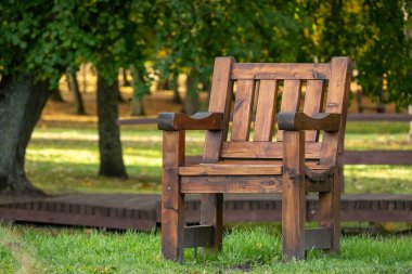 Dayanıklı ahşap bir bank güneşli bir parkta oturur, dinlenmeye, yansımaya ve huzurlu anlara davet eder yemyeşil ağaçlar ve çimenler arasında