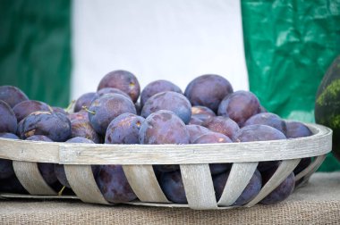 The plums, with their deep purple hues, are presented in a woven basket, creating a visually appealing arrangement. The scene is set on a burlap surface.