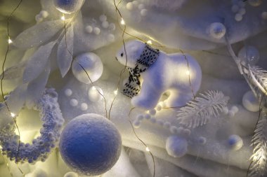 Eşarp takan pofuduk bir kutup ayısı biblosu karla kaplı süsler ve parıldayan peri ışıklarıyla çevrilidir, büyüleyici bir kış sahnesi yaratır.