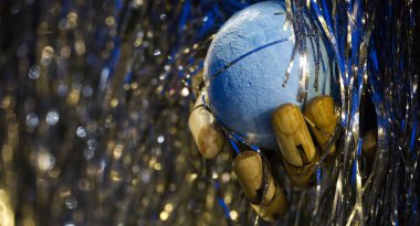 Yakın plan çekimde segmentli ahşap bir el nazikçe mavi bir küreyi kavrıyor, etrafında yumuşak, odaktan uzak bokeh gölgeleri olan şenlikli bir gümüş ve mavi süsleme var.