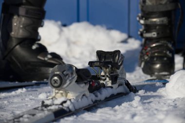 Taze karla kaplı siyah kayak botları ve bağlayıcılar da dahil olmak üzere kayak ekipmanlarının detaylı bir görüntüsü, yamaçlarda bir gün için hazırlanmayı öneriyor.