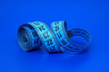 Esnek, mavi bir terzinin siyah işaretli mezurası parlak mavi bir zemin üzerine sarılmış ve açılarak, zanaat ve zindelik alanındaki faydasını vurguluyor.