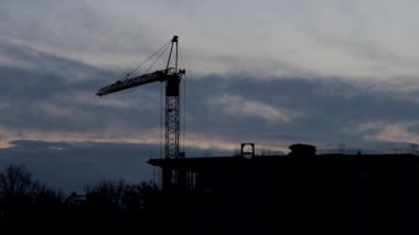 İkamet binasının tepesindeki işçilerin siluetleri. Arkaplanda inşaat vinci.