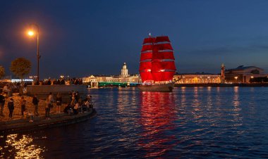 Rusya, St. Petersburg, deniz kenarındaki insanlar St. Petersburg gecesinin arka planına doğru yelken açan kırmızı yelkenli bir gemi gibi izliyorlar.