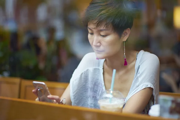 Una belleza asiática mirando el teléfono inteligente en la cafetería —  Fotos de Stock