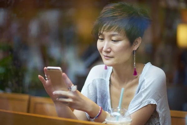 Smartphone kafede bakarak bir Asya Güzeli — Stok fotoğraf