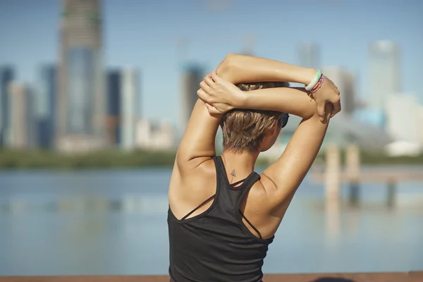 young woman stretching arms after jogging with skyline background