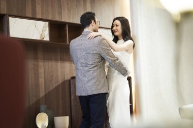 Bir çift Asyalı aşık oturma odasında dans ediyor ve gülümsüyor