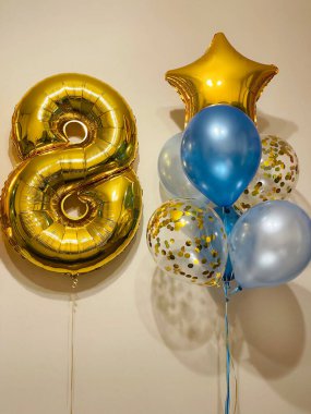 Bright composition of helium balloons in light blue, blue, golden colors, balloons with golden confetti and a large golden number eight