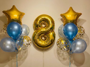 Composition of helium balloons in light blue, blue, golden colors, balloons with golden confetti and a large golden number eight