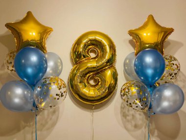 Composition of helium balloons in light blue, blue, golden colors, balloons with golden confetti and a large golden number eight