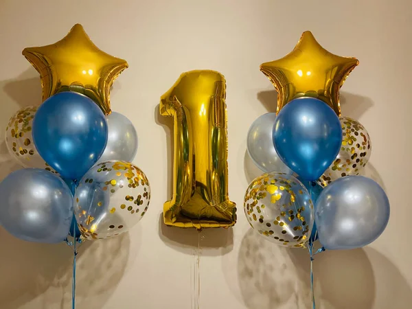 Bright composition of helium balloons in light blue, blue, golden colors, balloons with golden confetti and a large golden number one