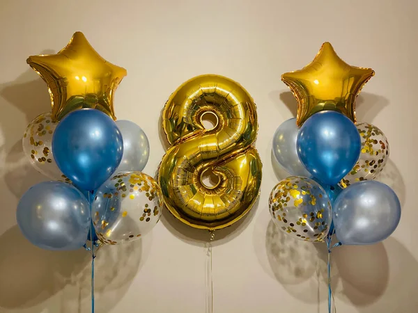 Bright composition of helium balloons in light blue, blue, golden colors, balloons with golden confetti and a large golden number eight