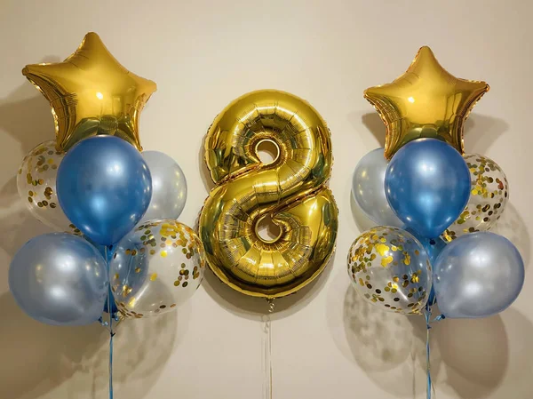 Composition of helium balloons in light blue, blue, golden colors, balloons with golden confetti and a large golden number eight