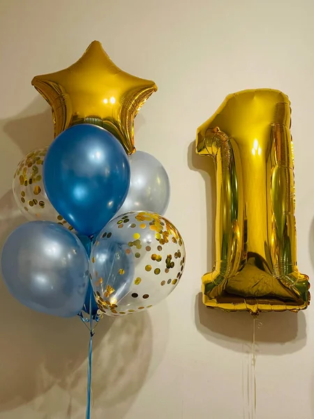 Composition of helium balloons in light blue, blue, golden colors, balloons with golden confetti and a large golden number one