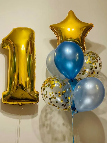 Bright composition of helium balloons in light blue, blue, golden colors, balloons with golden confetti and a large golden number one