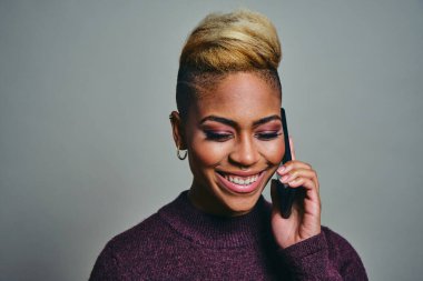 Gülümseyen genç bayan hippi gri arka planda akıllı telefon kullanırken gözlerini kaçırıyor.