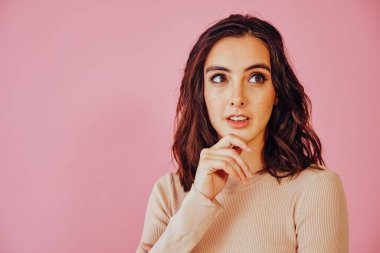 Elleri çenesinde, fotokopi çekilen pembe arka plana bakan düşünceli genç bir kadının stüdyo portresi. 