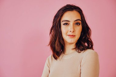 Pembe arka plan stüdyo portresindeki kameraya bakan düşünceli, güzel genç bayanı yakından çek.