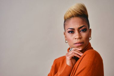 Kısa sarı saçlı, turuncu süveterli düşünceli genç bayan hippi gri arka plana bakıyor.