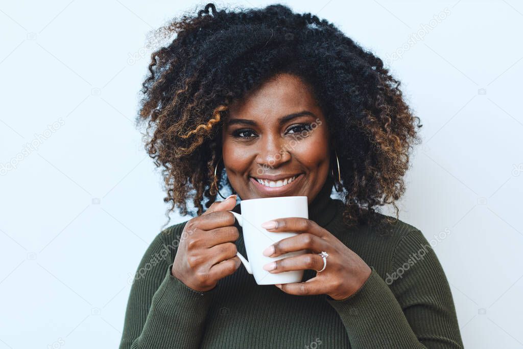 Portrait of smiling mid adult Afro woman drinking coffee against white background