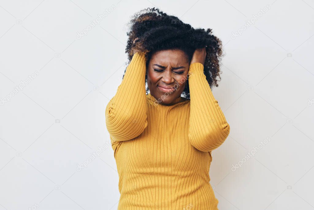 Woman with hand in hair struggling through headache. Yellow sweater. Eyes closed 