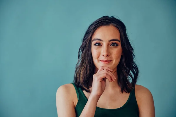 Thoughtful woman with hand on chin thinking on blue background wearing tank top