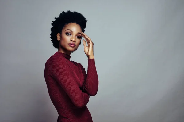 Kolları çaprazlanmış, bir eli şakakta duran güzel Afro-Amerikan bir kadının portresi.